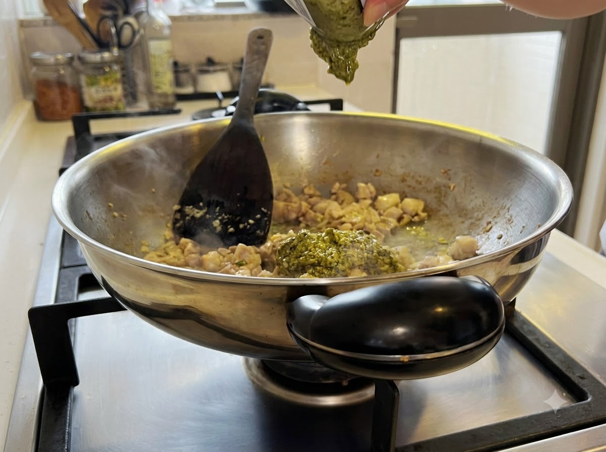 Salsa de pesto verde mezclándose con la mezcla de pollo y ajo dentro del wok.