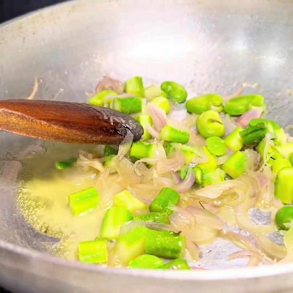 Cebollas salteadas y verduras verdes siendo retiradas de una sartén metálica con una cuchara de madera.
