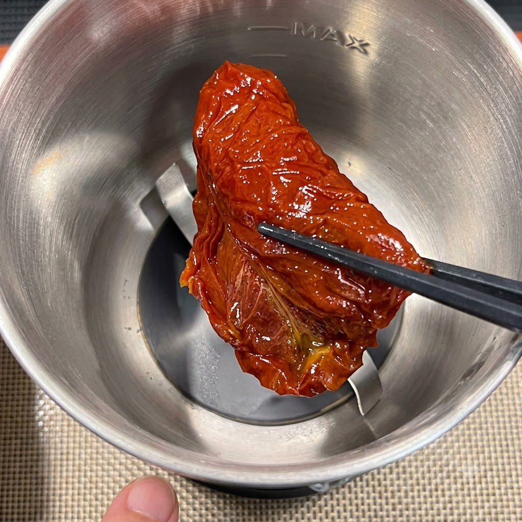 Una sola pieza de tomate seco siendo colocada en el accesorio de un procesador de alimentos de acero inoxidable usando palillos.