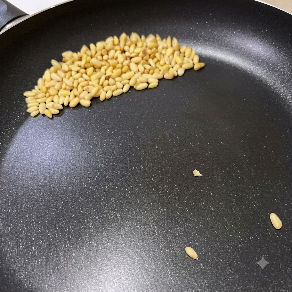 Piñones dorándose en una sartén seca durante la preparación de la pasta al pesto italiano.