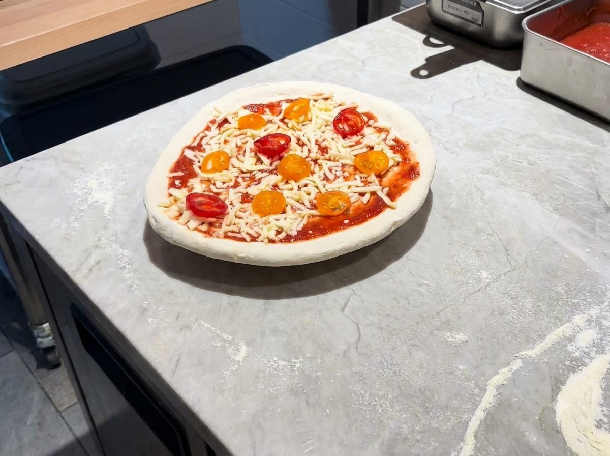 Una pizza completamente ensamblada reposando sobre una pala metalica en una encimera de marmol.