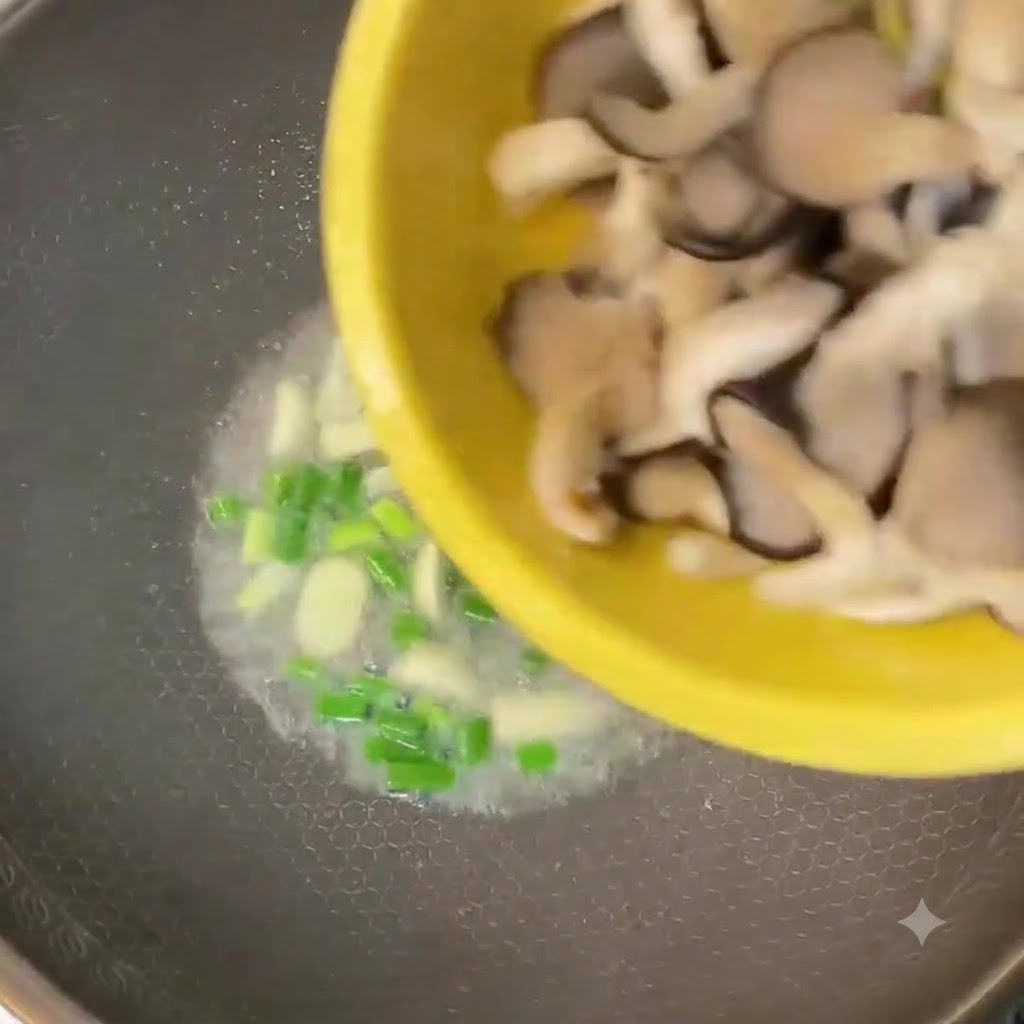 Champiñones ostra picados siendo vertidos desde un tazón amarillo a un wok con cebolla verde y ajo.