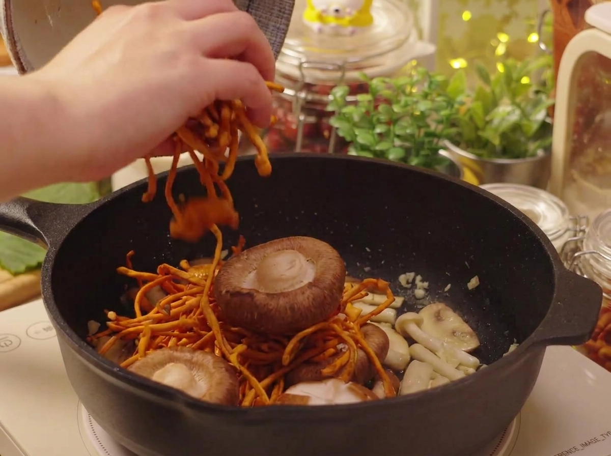 Champiñones shiitake y cordyceps rehidratados siendo añadidos a la sartén.