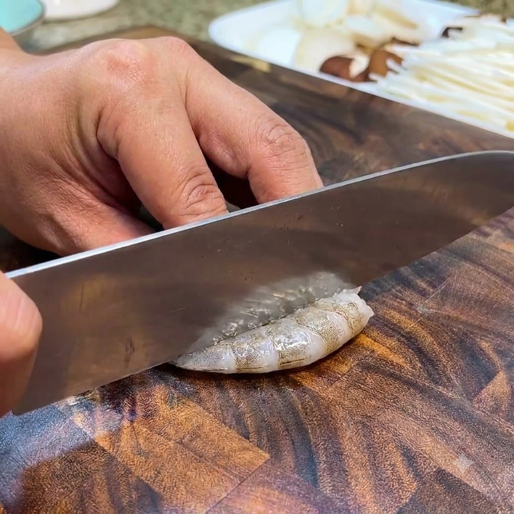 Camarones crudos siendo limpiados y desvenados con un cuchillo en una tabla de cortar de madera.