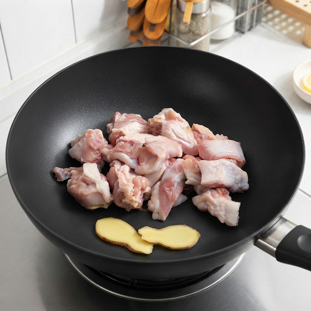 Trozos de pollo crudo y rodajas de jengibre reposando en un wok antes de freír.