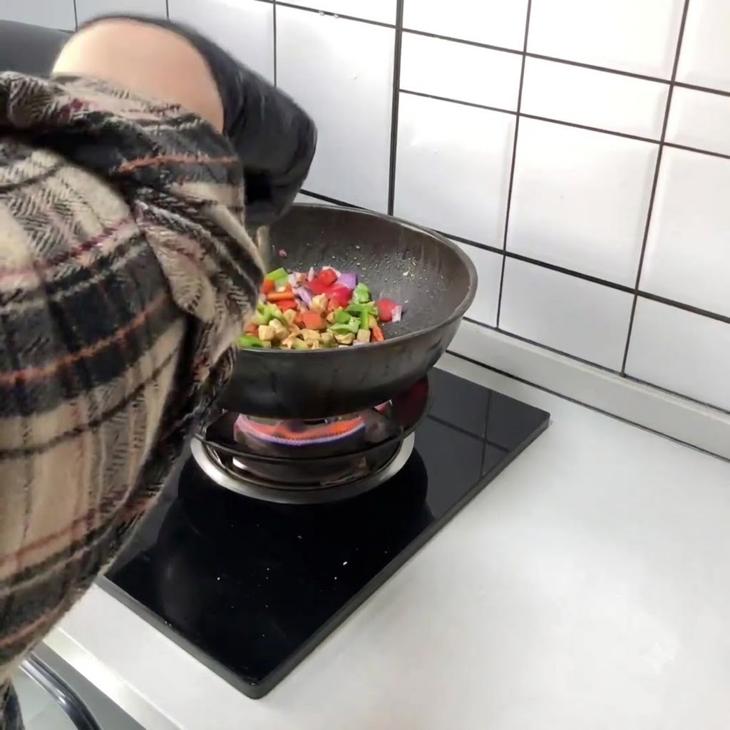 Pimientos rojos y verdes picados siendo añadidos directamente al wok que contiene el pollo salteado.