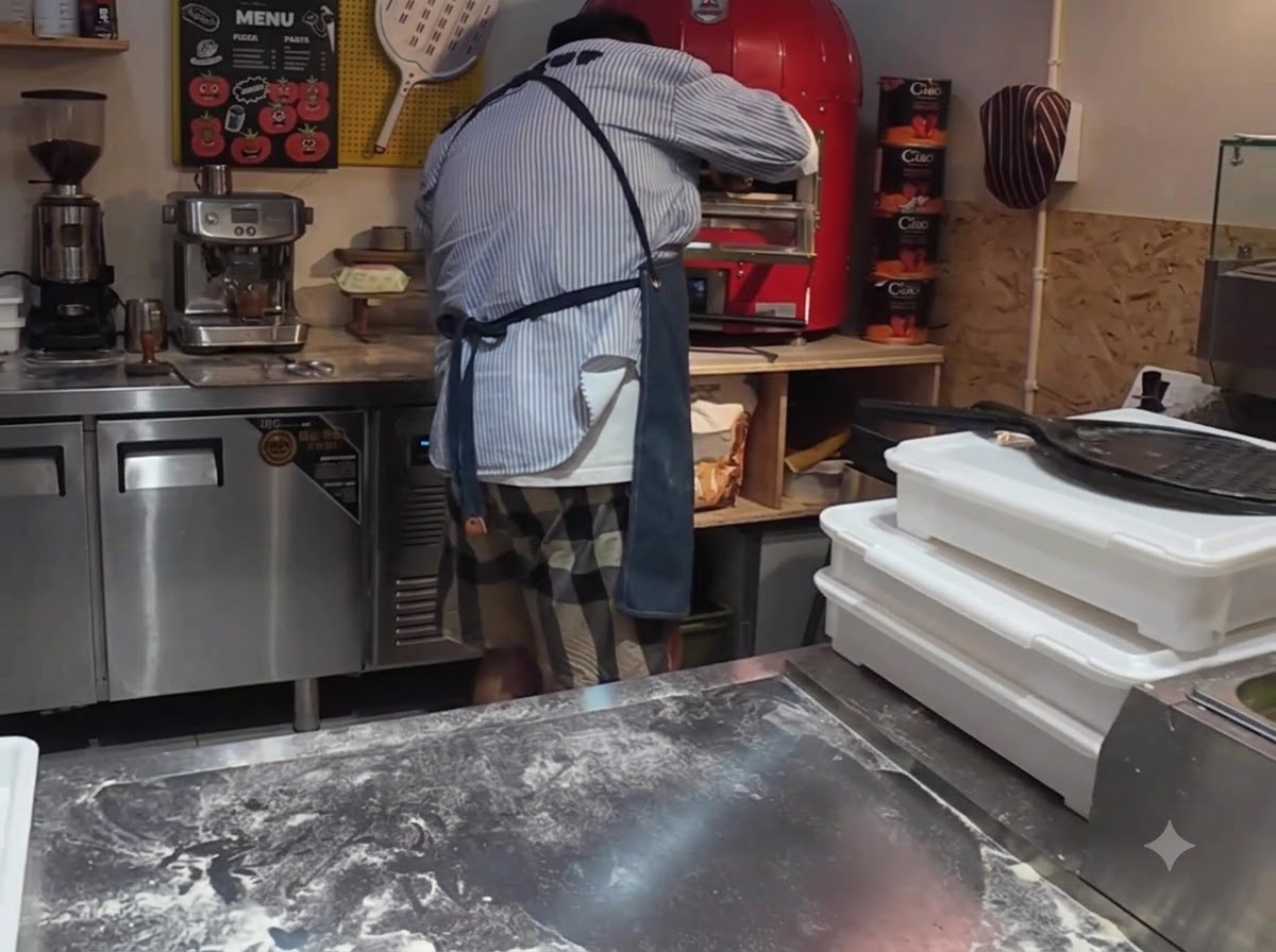 Una pizza siendo introducida en un horno de pizza eléctrico comercial de color rojo brillante utilizando una pala para pizza.