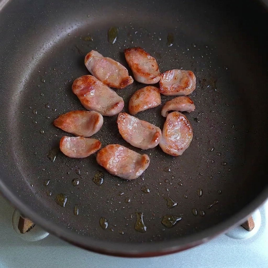 Rodajas de salchicha y trozos de ajo mezclándose juntos en una sartén.