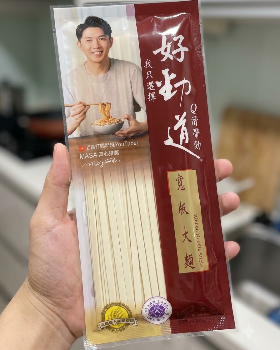 Un paquete de fideos anchos en tiras Hao Jin Dao sostenido frente a un fondo de cocina.