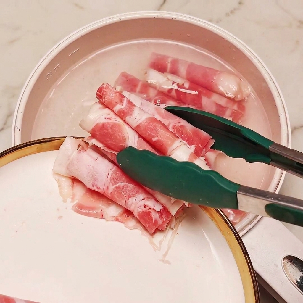 Ternera en rodajas congelada siendo introducida con pinzas en una olla con agua hirviendo y secciones de cebollino.