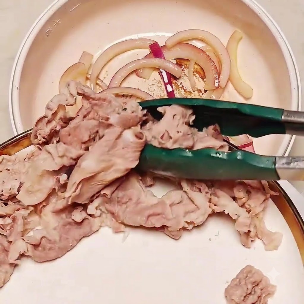 Rodajas de ternera blanqueadas siendo transferidas con pinzas a una sartén que contiene cebollas salteadas.