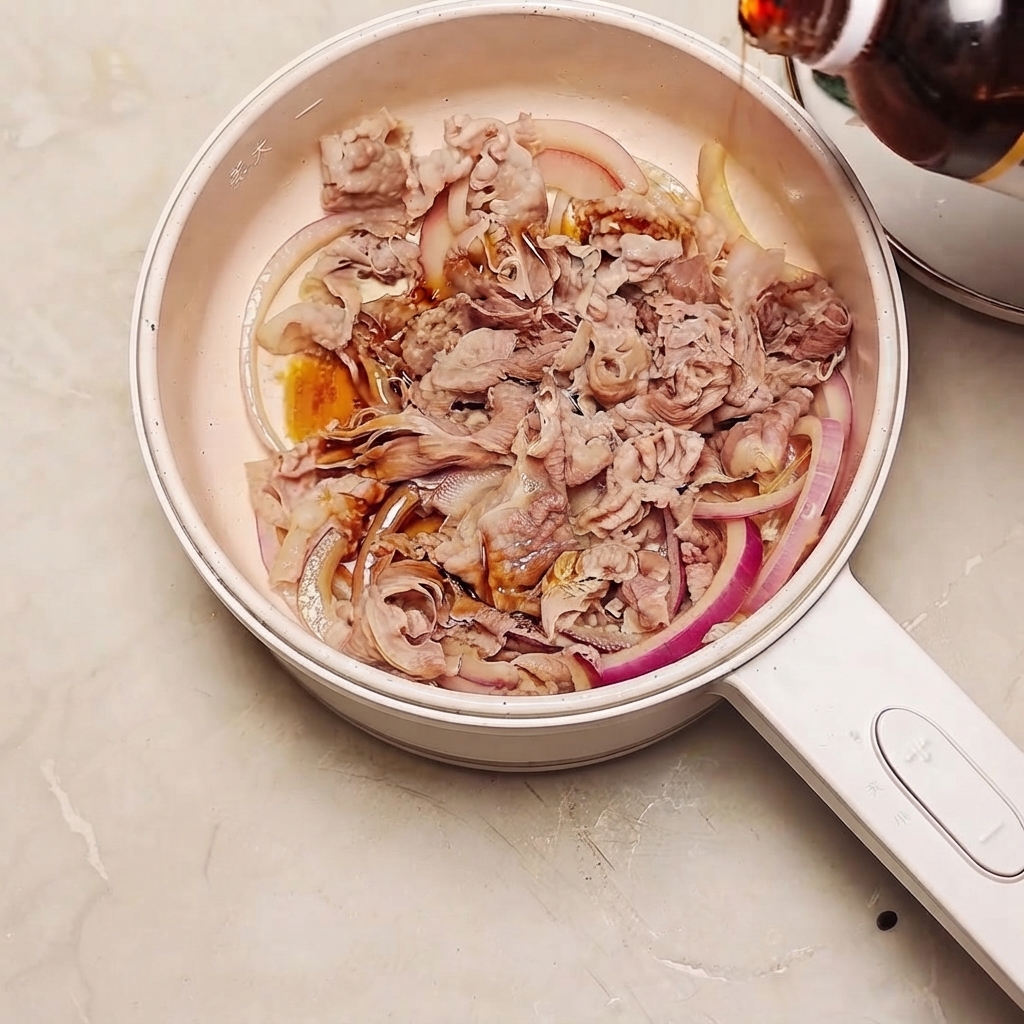 Salsa sukiyaki siendo vertida desde una botella en una sartén llena de ternera y rodajas de cebolla roja.