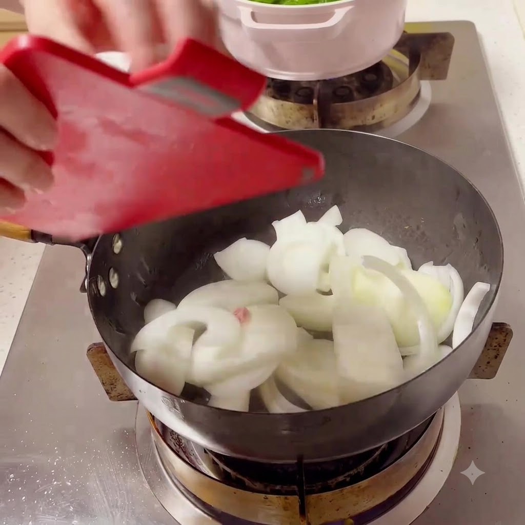 Rodajas de cebolla blanca siendo vertidas desde una tabla de cortar roja en un wok negro caliente sobre la hornilla.
