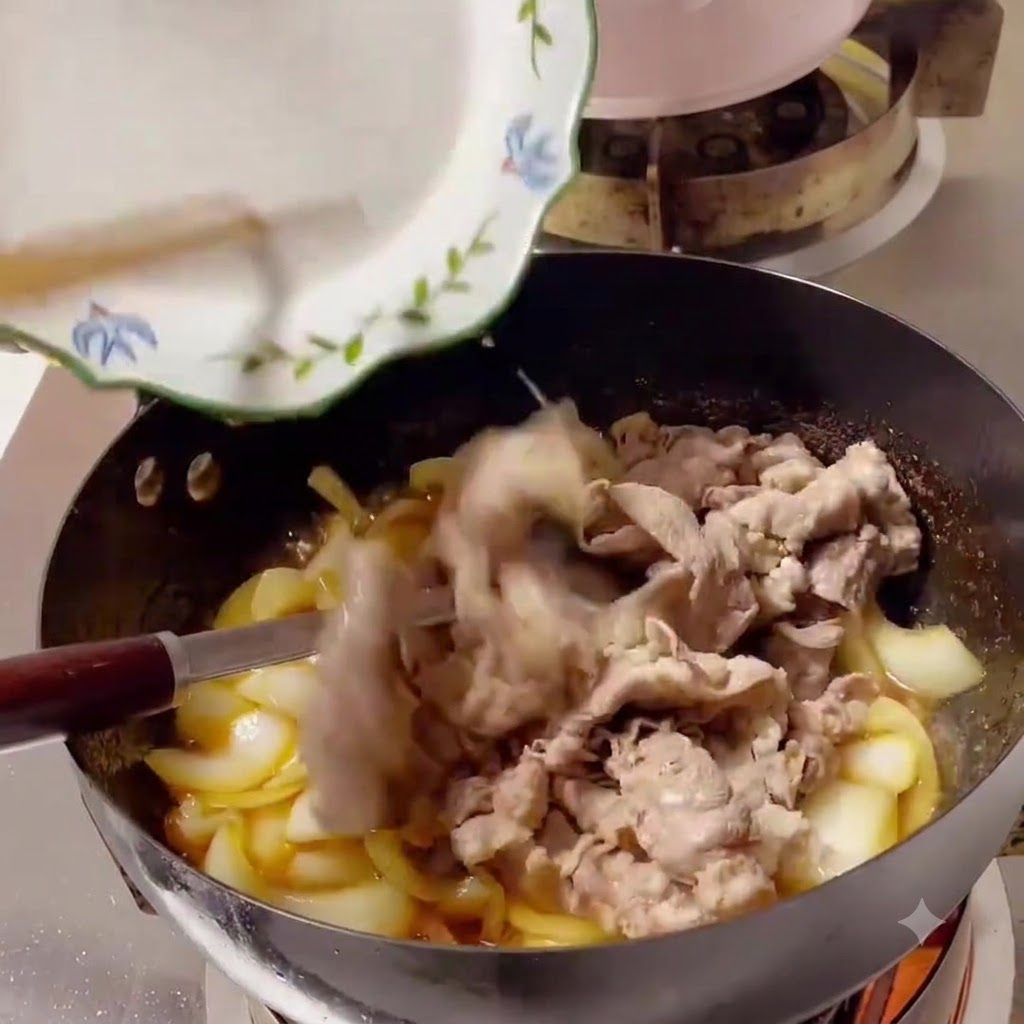 Lonchas de ternera cocida deslizándose desde un plato blanco hacia un wok lleno de cebollas y salsa.