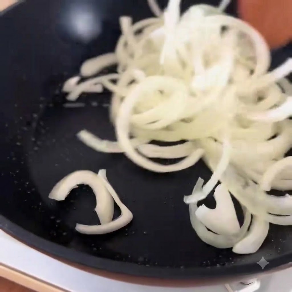 Láminas de ternera blanqueadas echándose sobre cebollas cocinadas en una sartén.