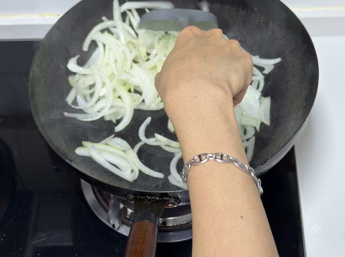 Una persona utilizando una espátula para saltear cebollas cortadas en un wok, mostrando trozos translúcidos y ligeramente dorados.