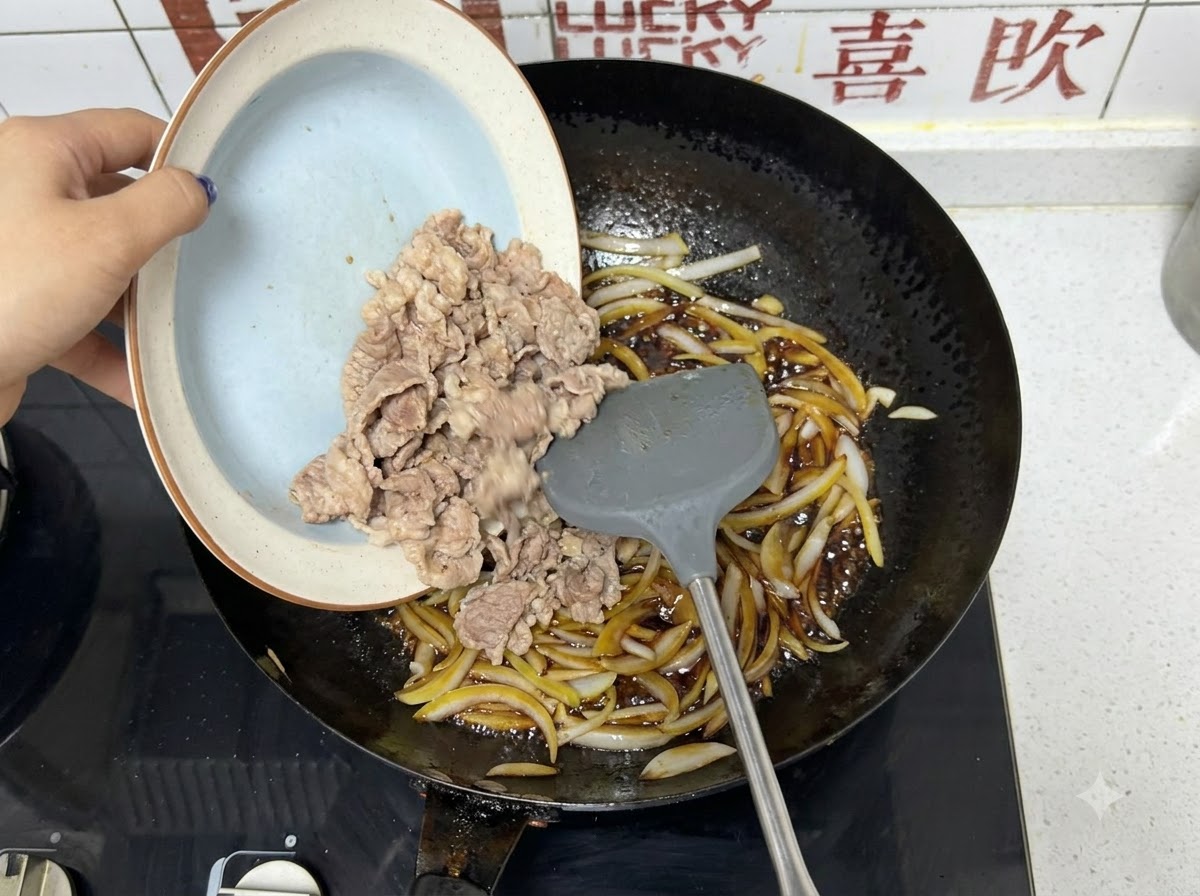 Láminas de ternera preblanqueadas deslizándose desde un plato hacia un wok con cebollas y salsa oscura.