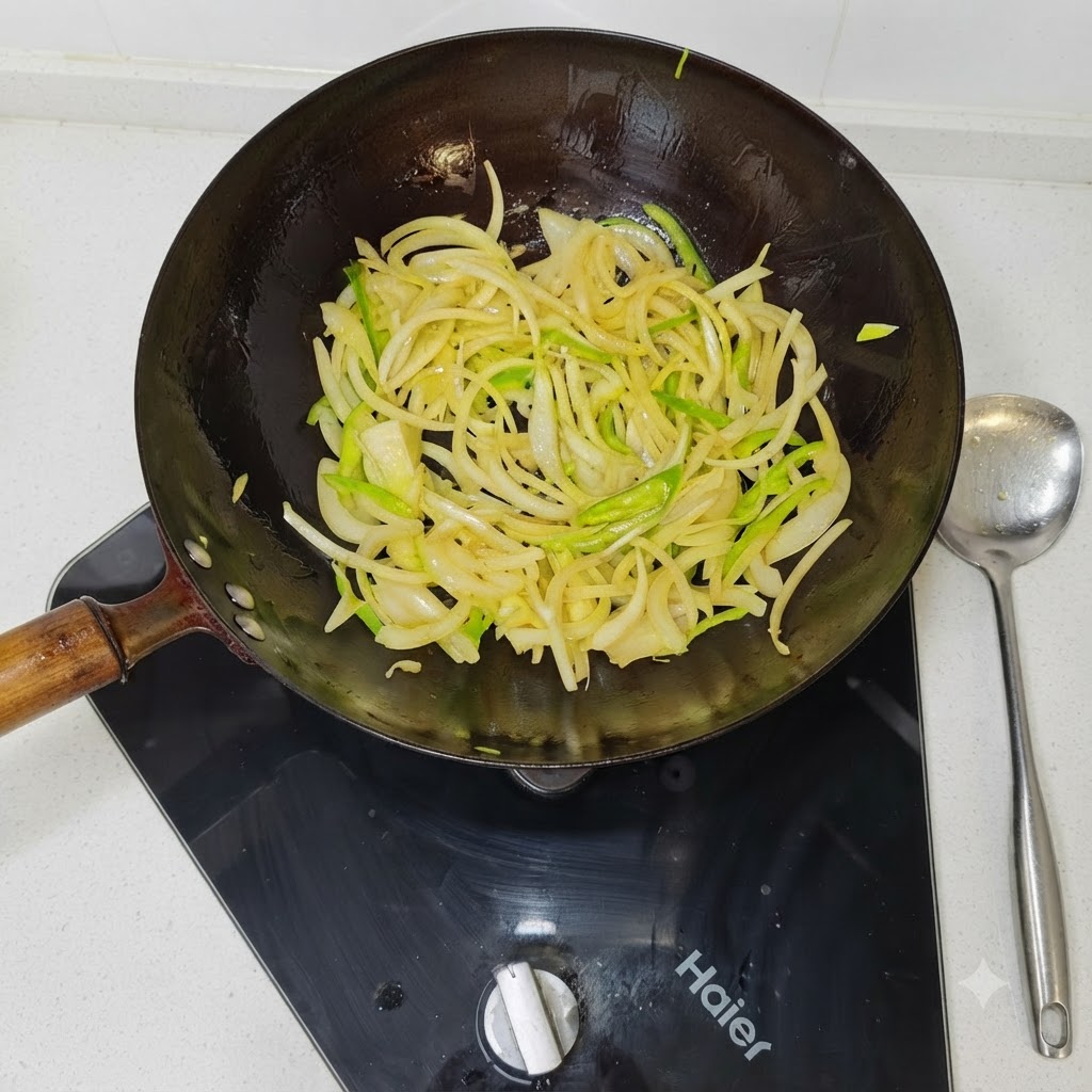 Tiras de cebolla y pimientos verdes salteándose en el interior de un wok negro caliente.