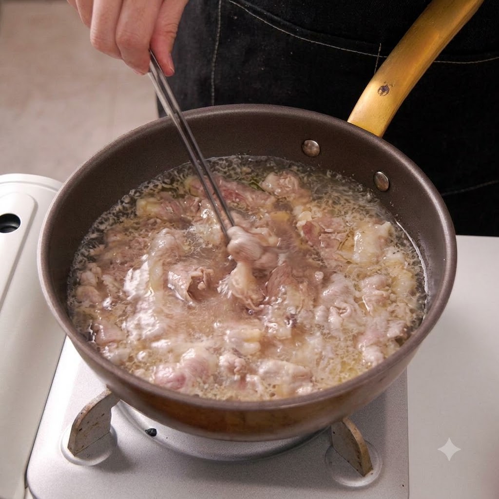Unas pinzas de cocina retirando láminas de ternera escaldada del agua hirviendo.