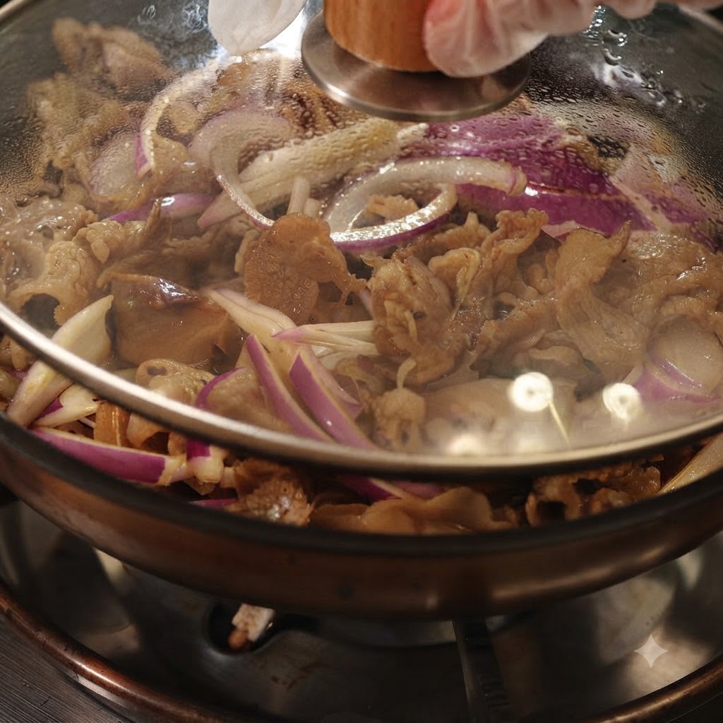 Una sartén tapada con una tapa de cristal transparente, mostrando carne y cebollas moradas cocinándose a fuego lento en su interior.