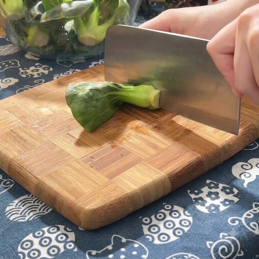 Brotes verdes cortados en trozos pequeños sobre una tabla de cortar de madera utilizando una cuchilla pesada.