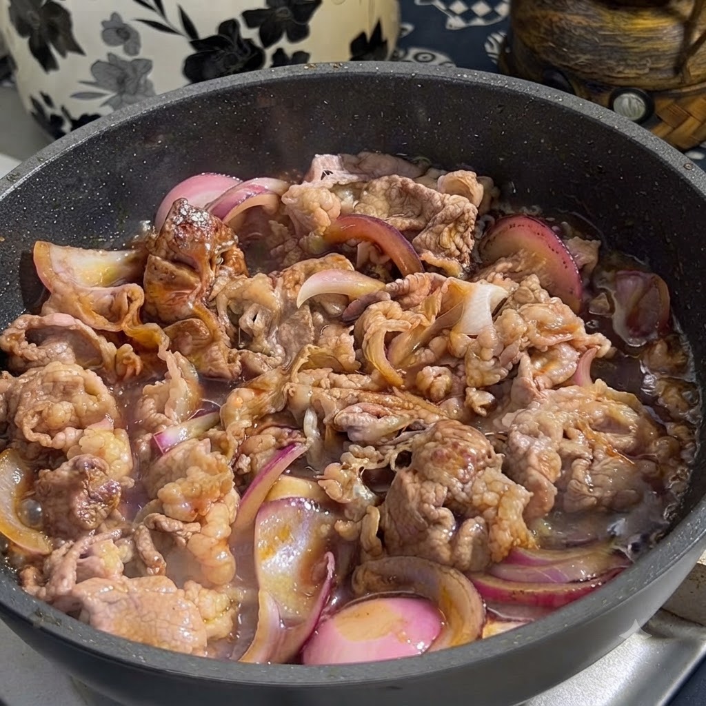 Salsa teriyaki vertida desde un recipiente en una sartén con ternera dorada y rodajas de cebolla morada.