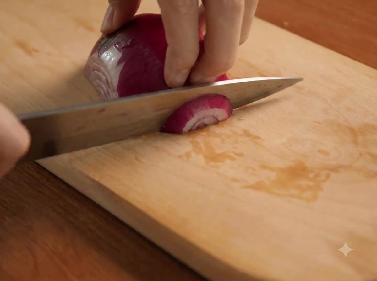 Una cebolla morada siendo cortada finamente con un cuchillo sobre una tabla de madera.