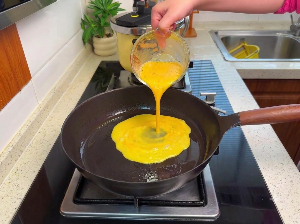 Huevos batidos siendo vertidos en una sartén caliente sobre una estufa, formando cuajada suave a fuego lento.
