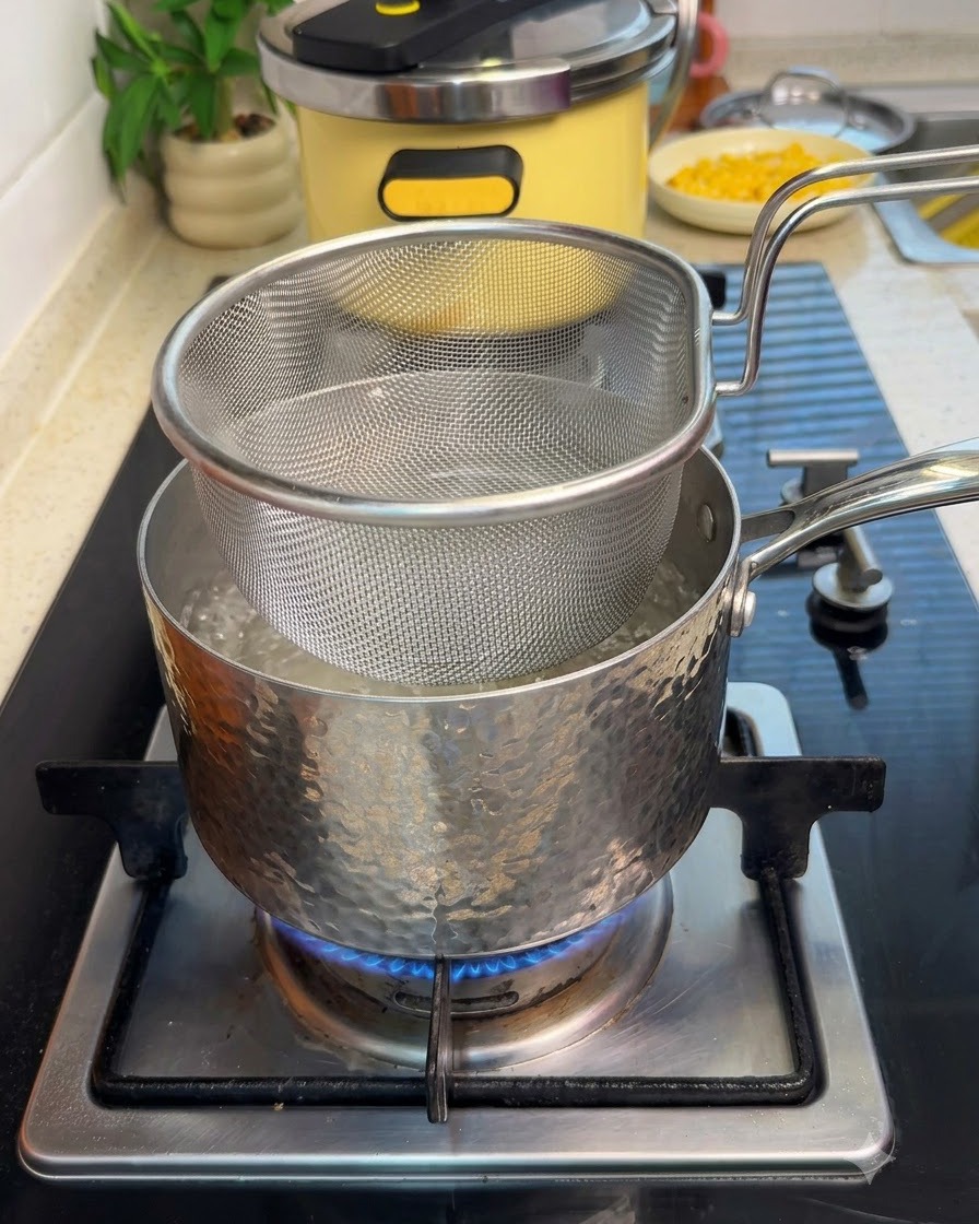 Una cesta colador de malla sumergida en una olla con agua hirviendo en la estufa con carne de res en rodajas.
