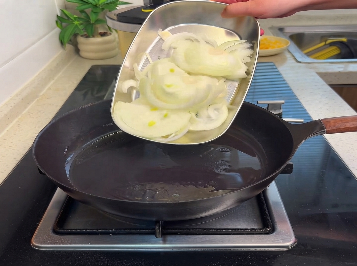 Cebollas cortadas siendo deslizadas desde una bandeja de metal hacia una sartén caliente con aceite.