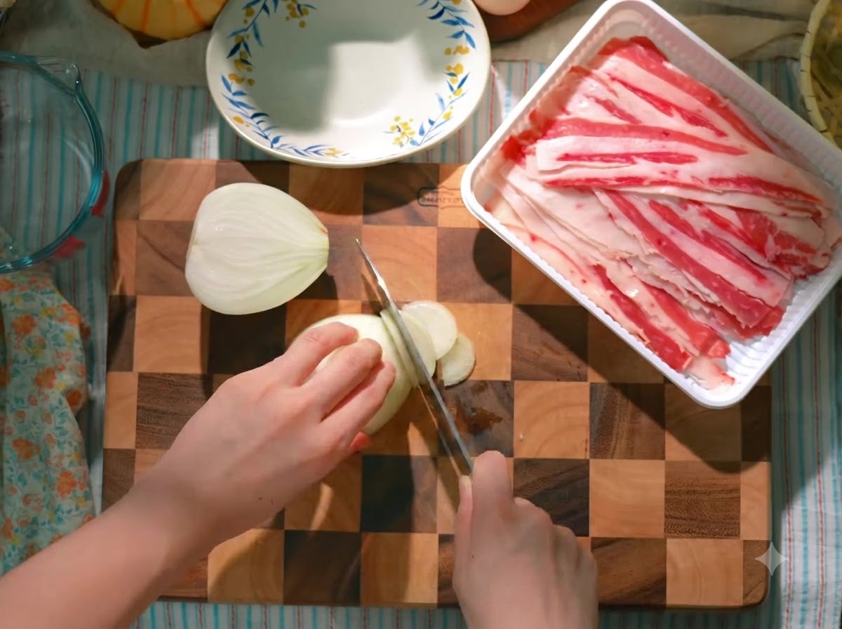 Una cebolla siendo cortada cuidadosamente en una tabla de madera junto a una bandeja de tiras de ternera cruda.