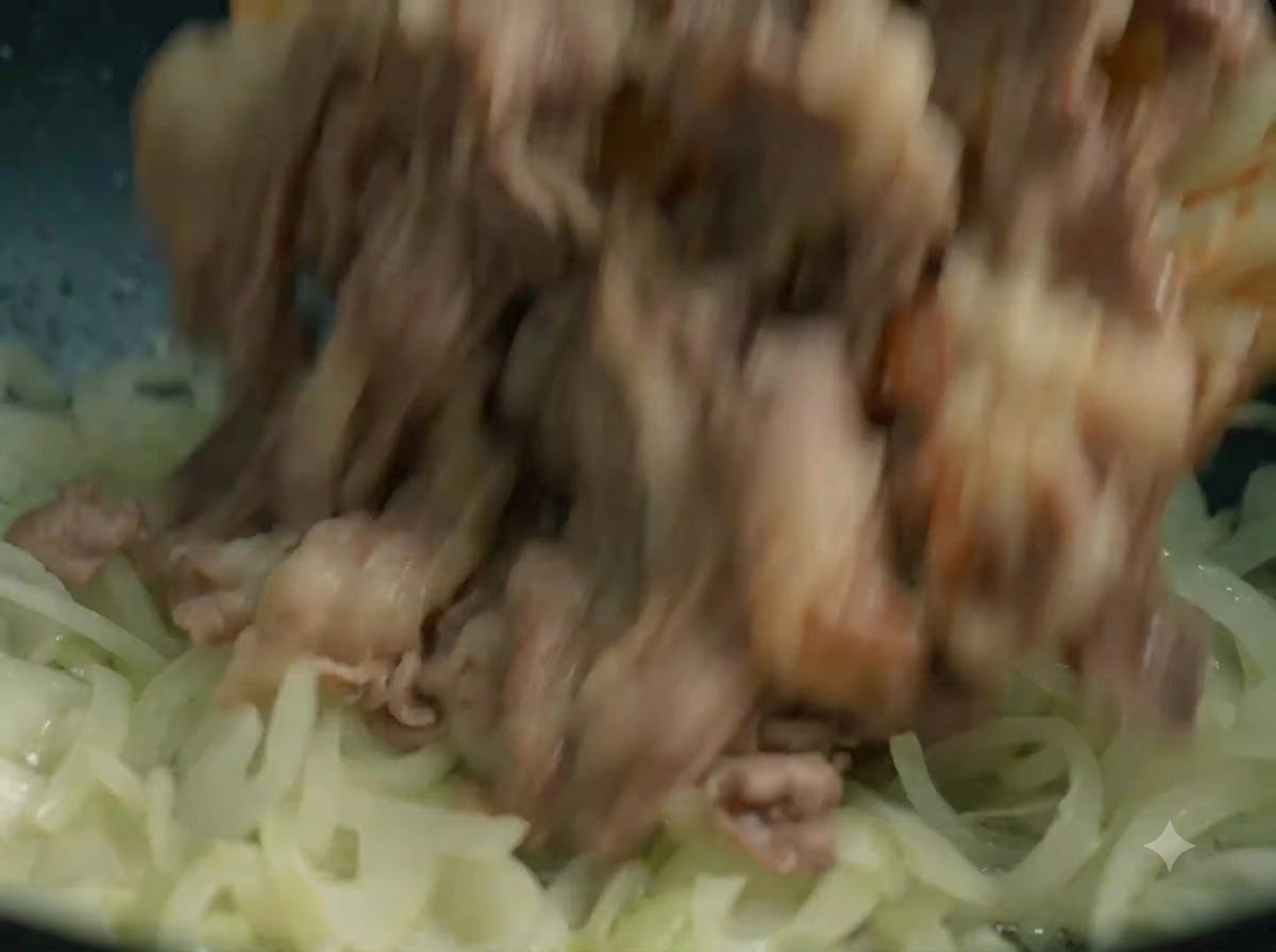 Tiras de ternera cocinada añadiéndose de nuevo a la sartén con la cebolla pochada.