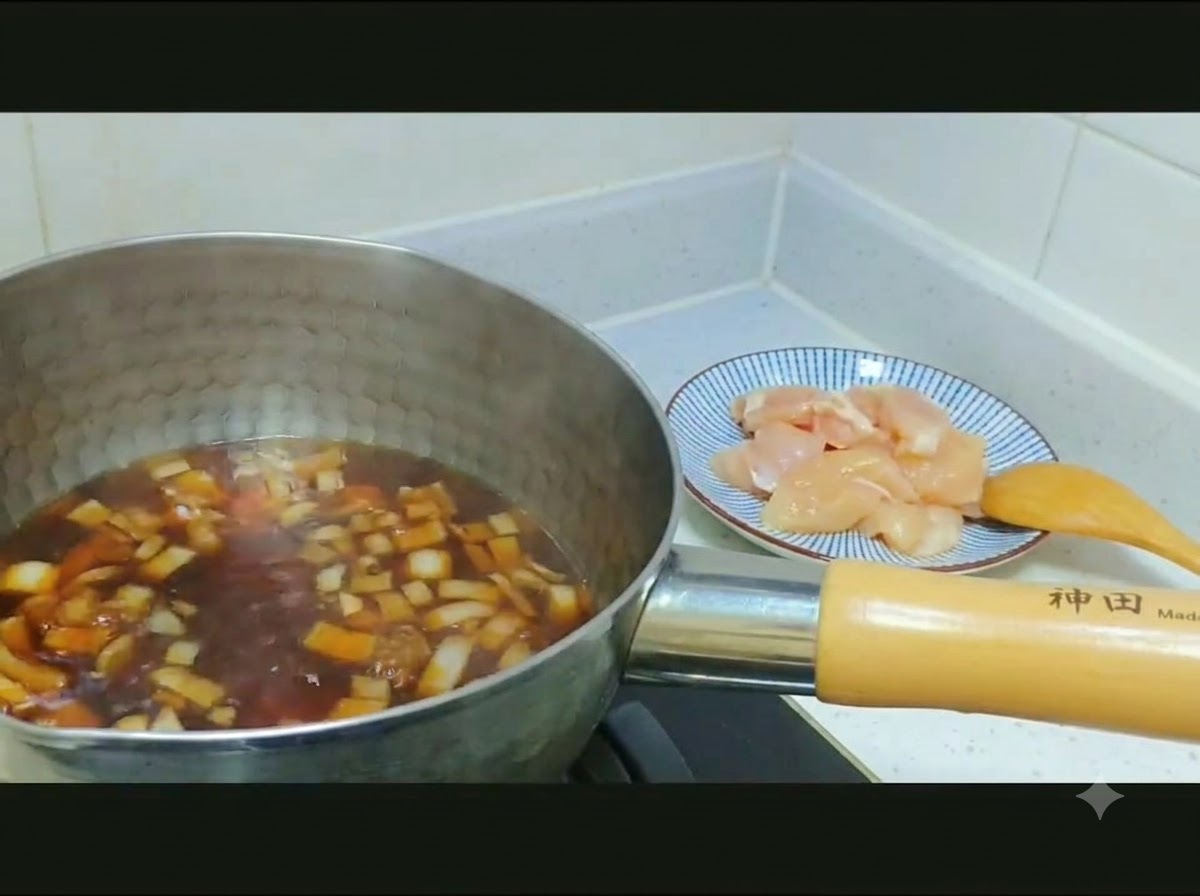 Pollo crudo en dados y cebollas en rodajas siendo transferidos desde un plato con patrones hacia una olla de caldo oscuro.
