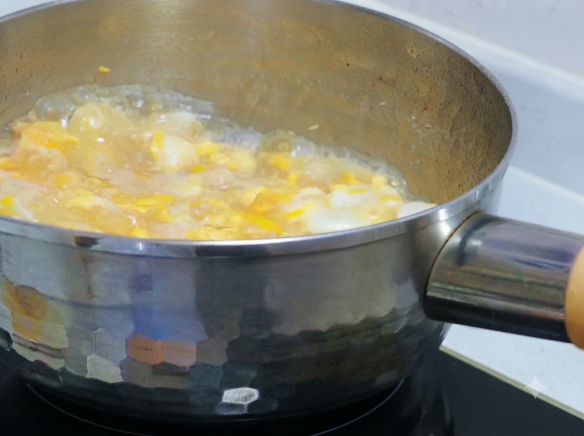 Líquido de huevo parcialmente batido siendo vertido sobre pollo y cebollas a fuego lento en una olla.
