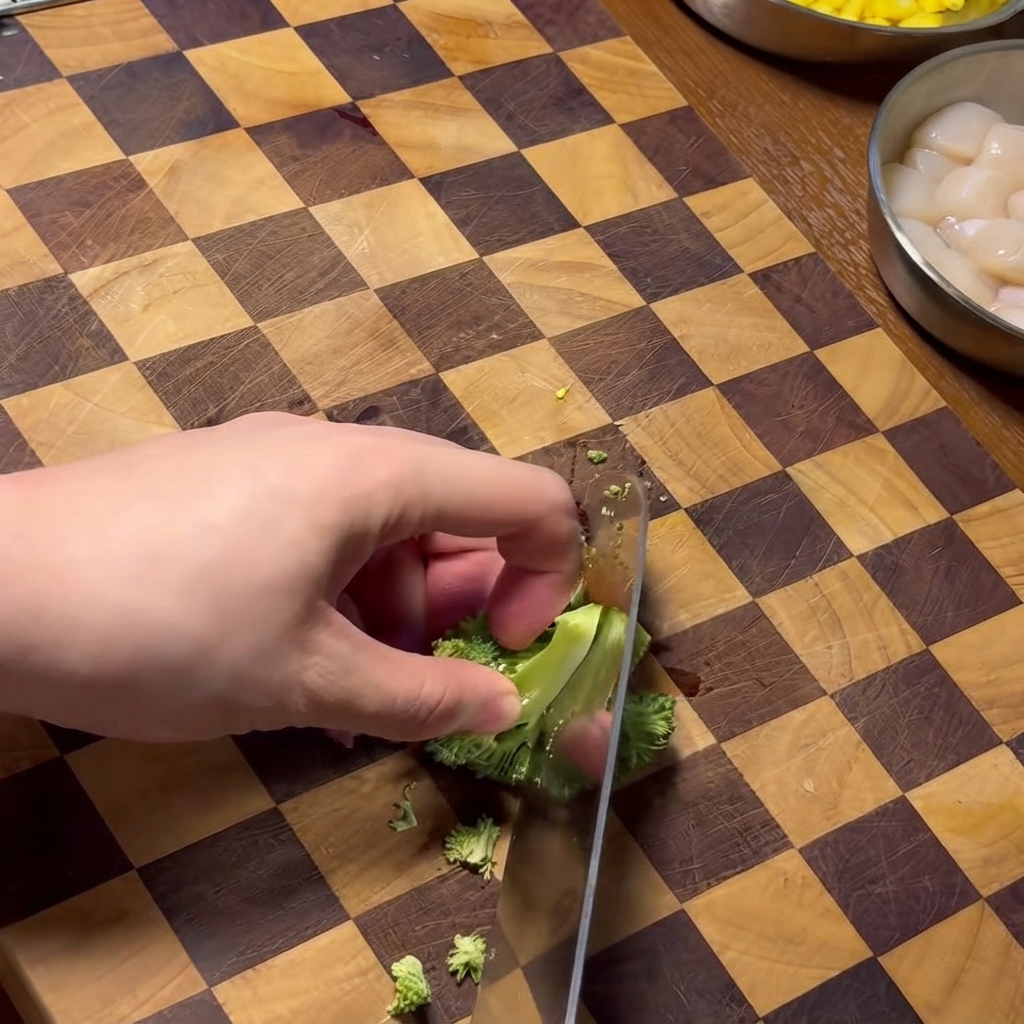 Una mano usando un cuchillo para picar floretes de brócoli en una tabla de cortar de madera a cuadros.