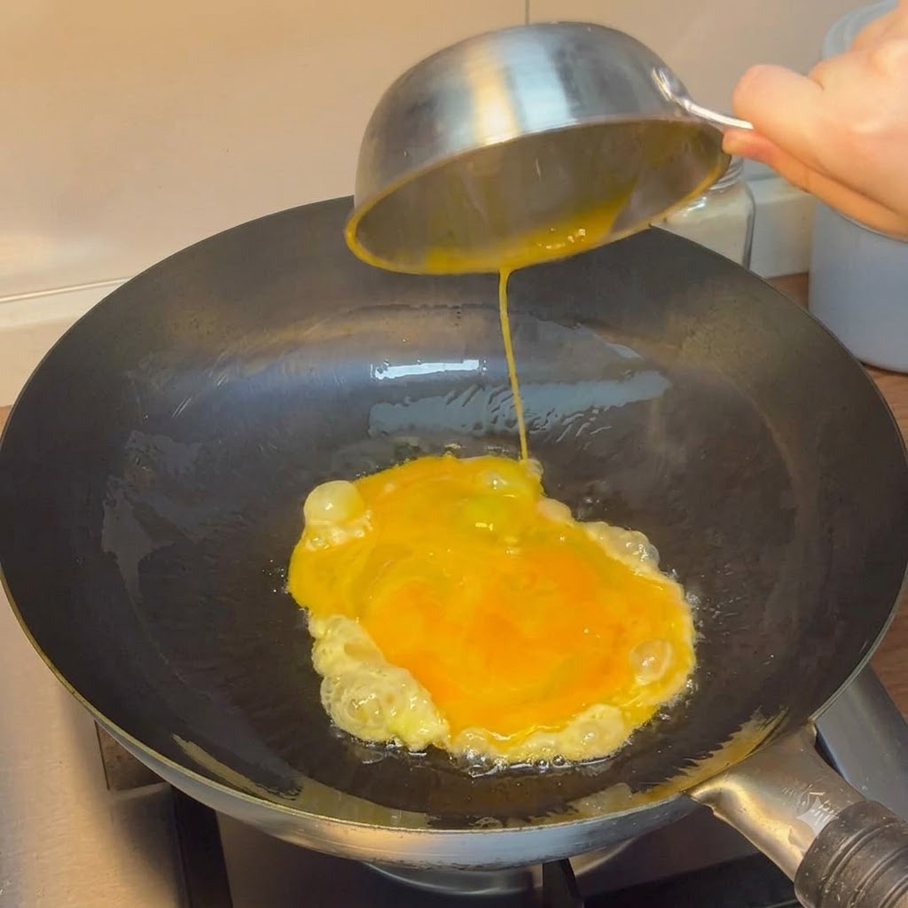 Huevos batidos vertiéndose desde un tazón de acero en un wok caliente.