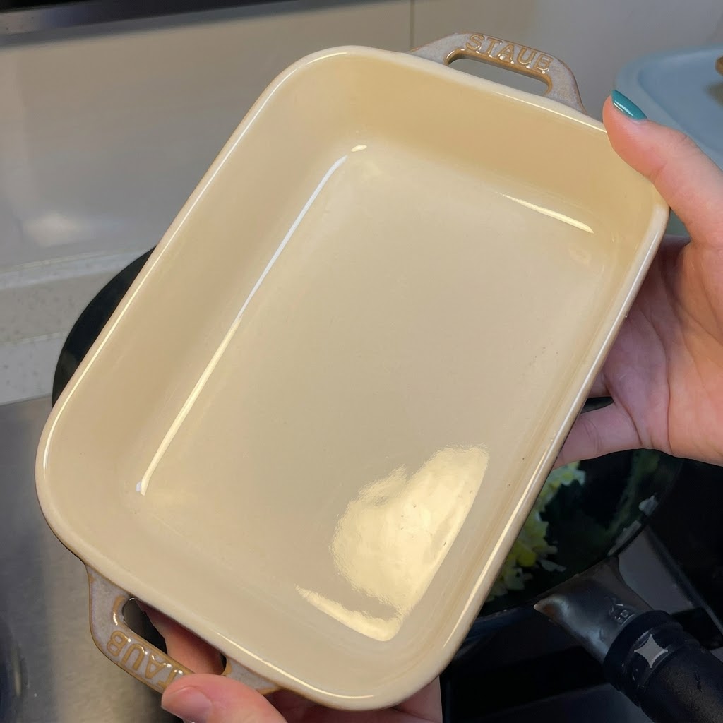 Una persona sosteniendo una fuente de horno de cerámica blanca rectangular y vacía sobre un wok que contiene arroz frito con huevo.