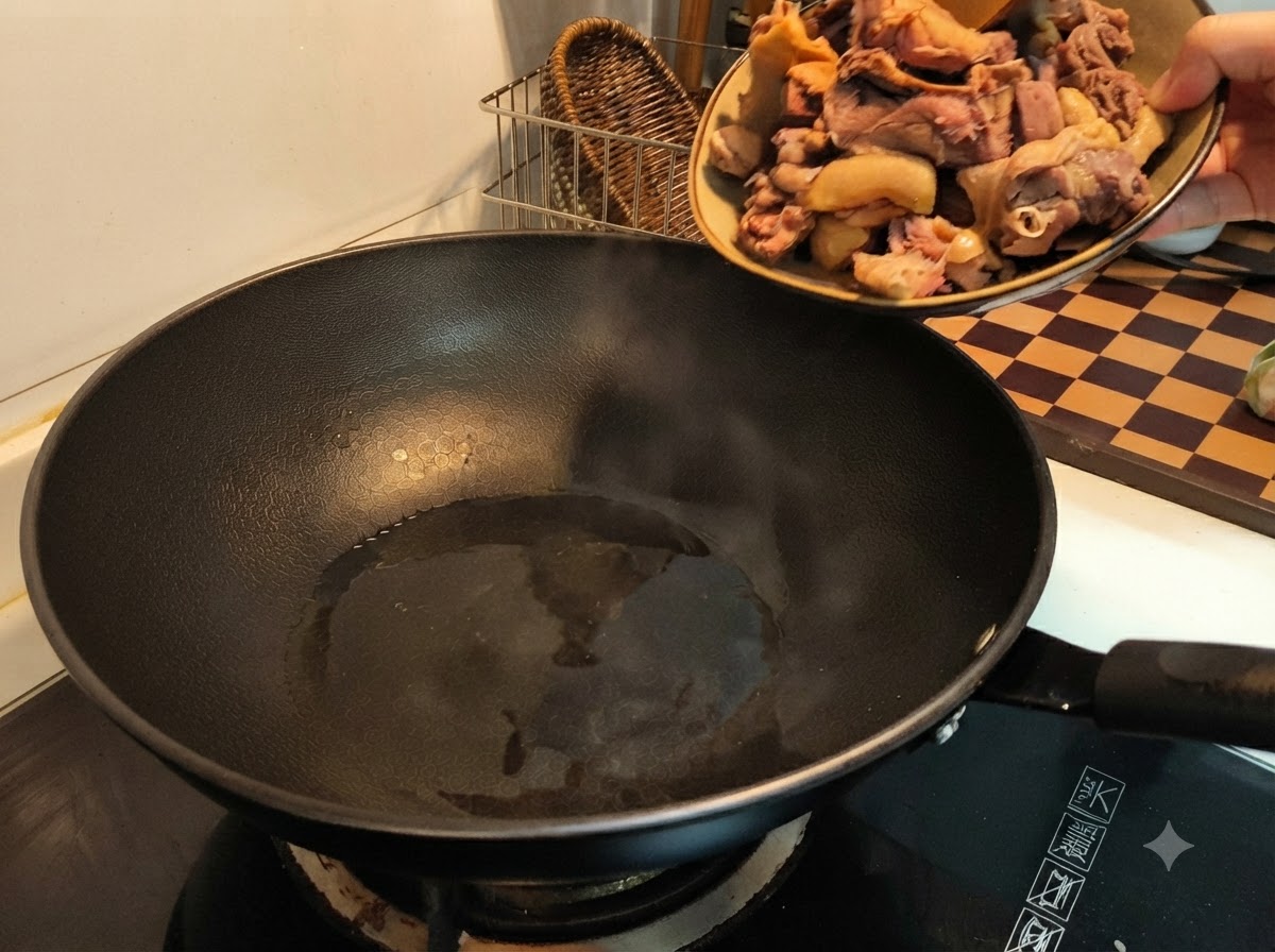 Una mano vertiendo trozos de pato blanqueados desde un plato a un wok negro caliente con aceite.