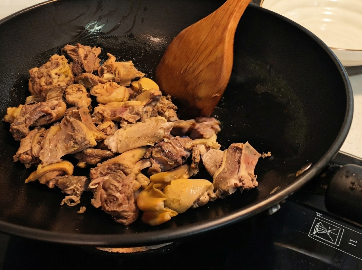 Trozos de pato siendo salteados en un wok con una espátula de madera, mostrando la piel dorada.