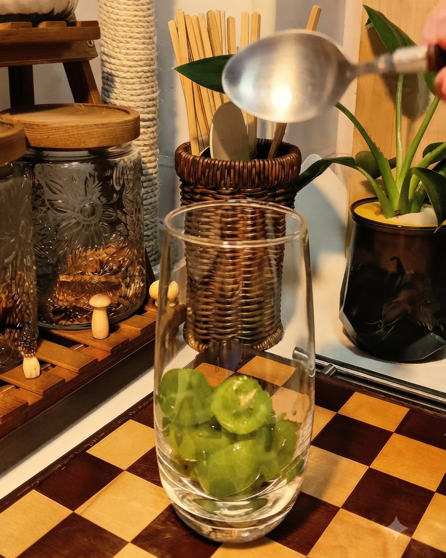 Uvas verdes frescas siendo aplastadas por una cuchara en el fondo de un vaso alto y transparente.