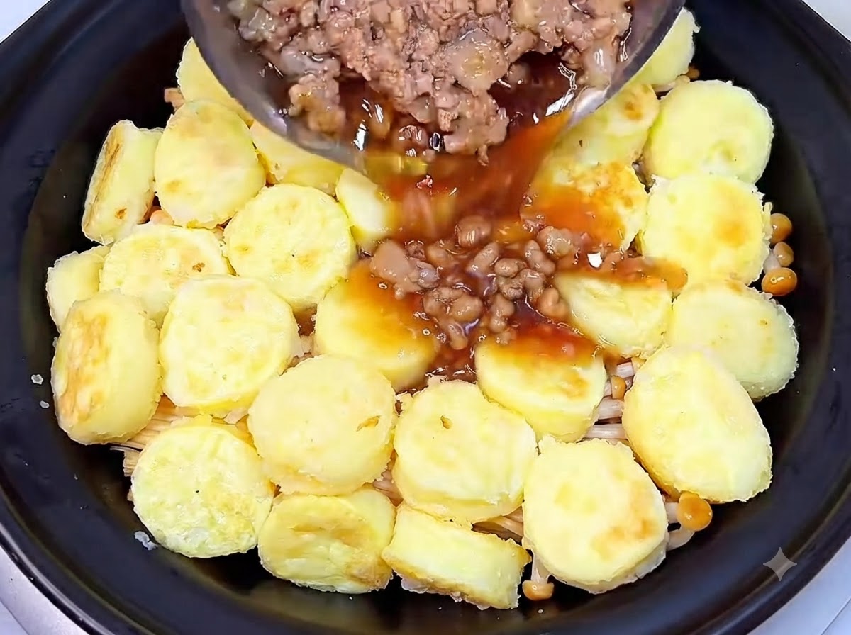 Carne de cerdo picada cocinada y salsa oscura sabrosa siendo vertidas desde una sartén sobre la capa de tofu dentro de la olla de barro.
