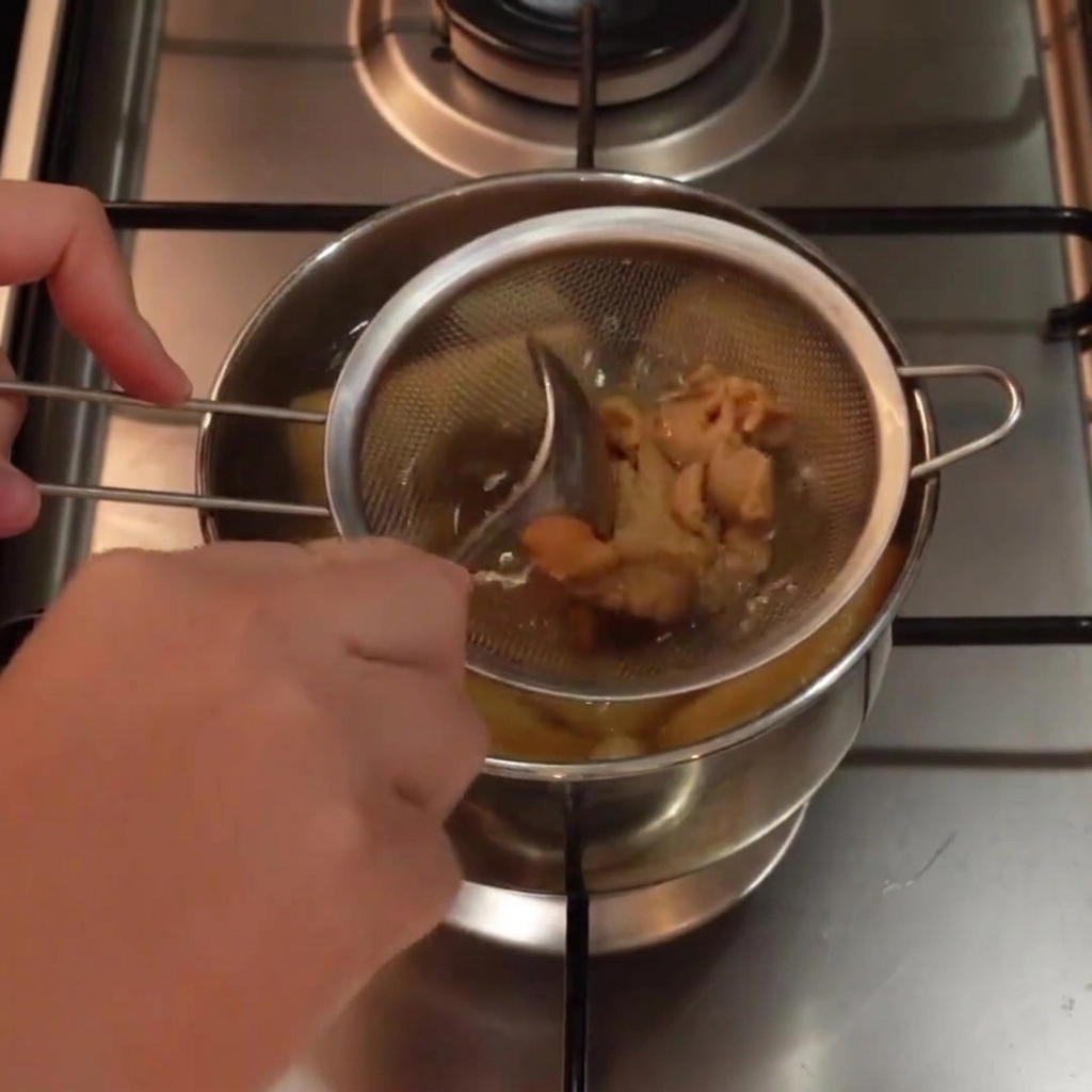 Pasta de miso blanco siendo mezclada dentro de un colador de metal sumergido en una olla de sopa caliente usando una cuchara.
