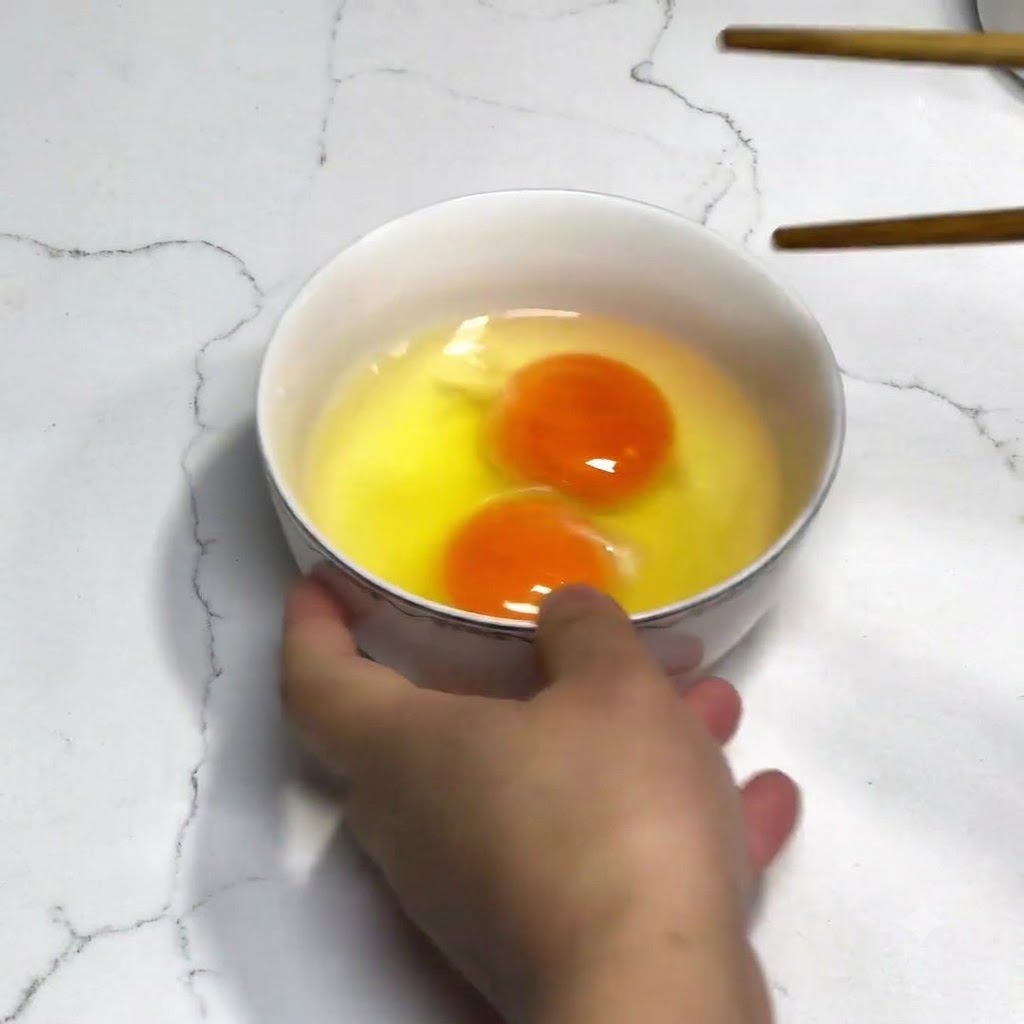 Dos huevos frescos en un bol blanco siendo batidos con palillos de madera sin condimentos.
