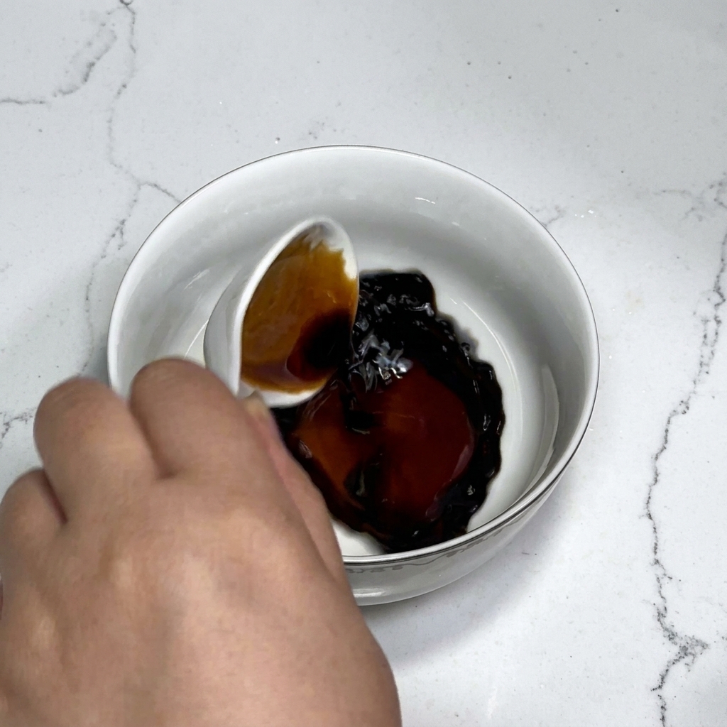 Ingredientes de la salsa, incluyendo salsa de soja, salsa de ostras, azúcar y almidón, siendo revueltos con agua en un bol blanco con una cuchara.
