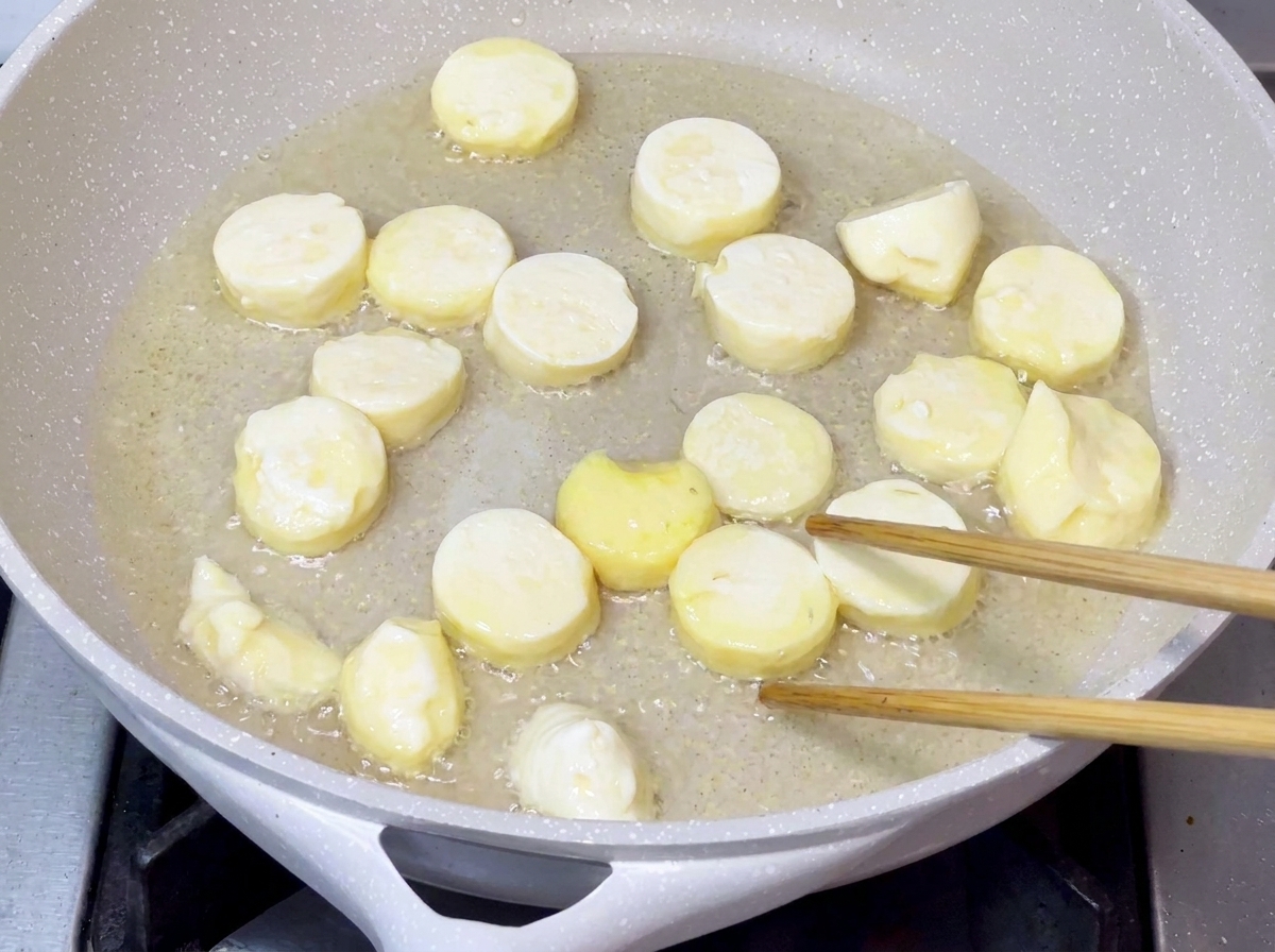 Trozos de tofu friéndose en aceite caliente en una sartén hasta que sus superficies se vuelven doradas y crujientes.