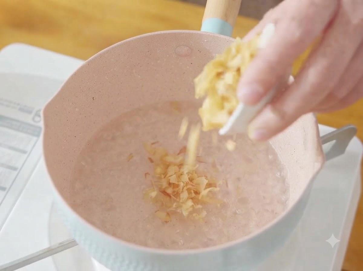 Un puñado de copos de bonito secos cayendo en una olla con agua hirviendo.