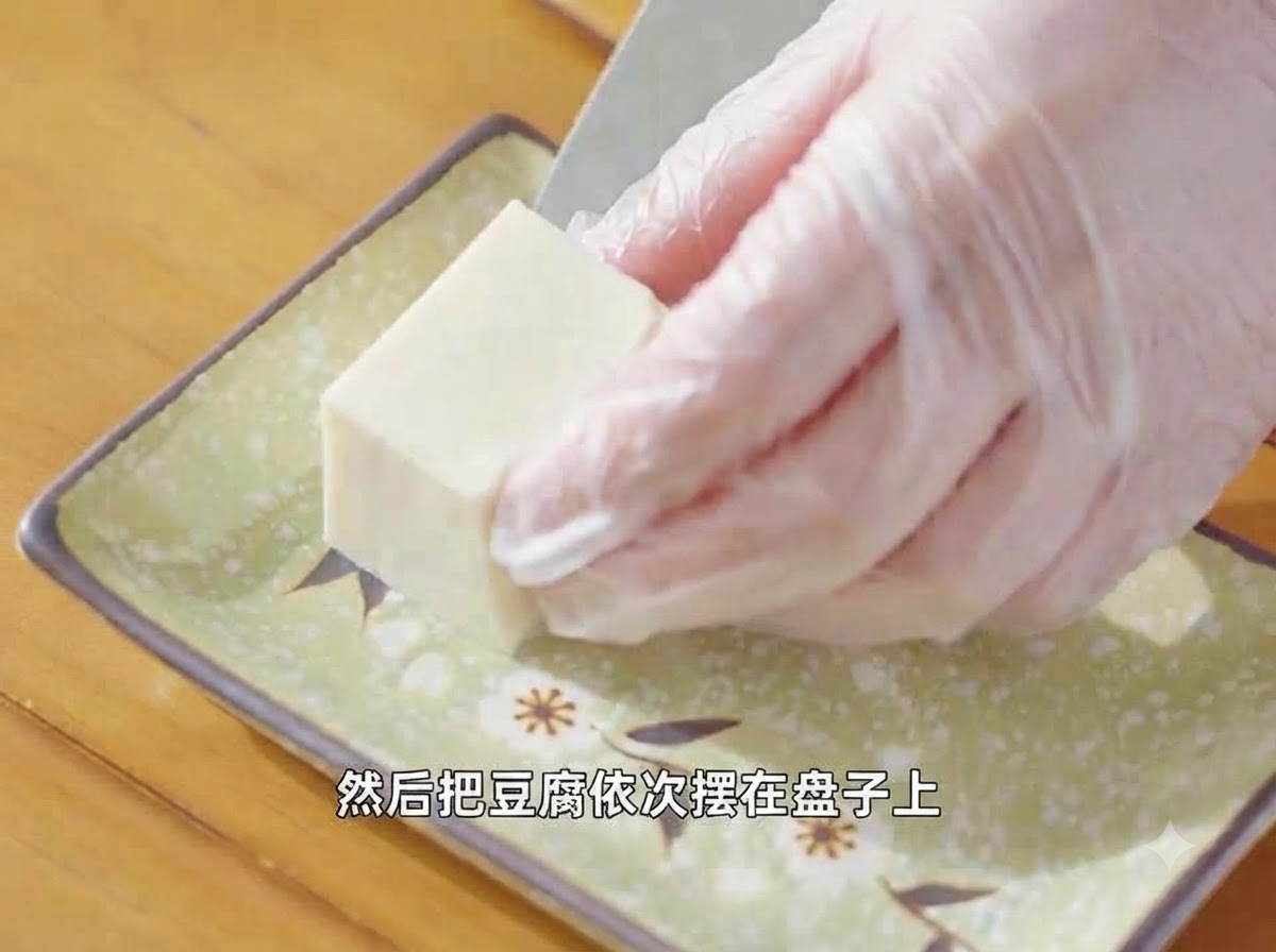 Manos con guantes organizando un trozo de tofu sedoso cortado en un plato verde decorativo.