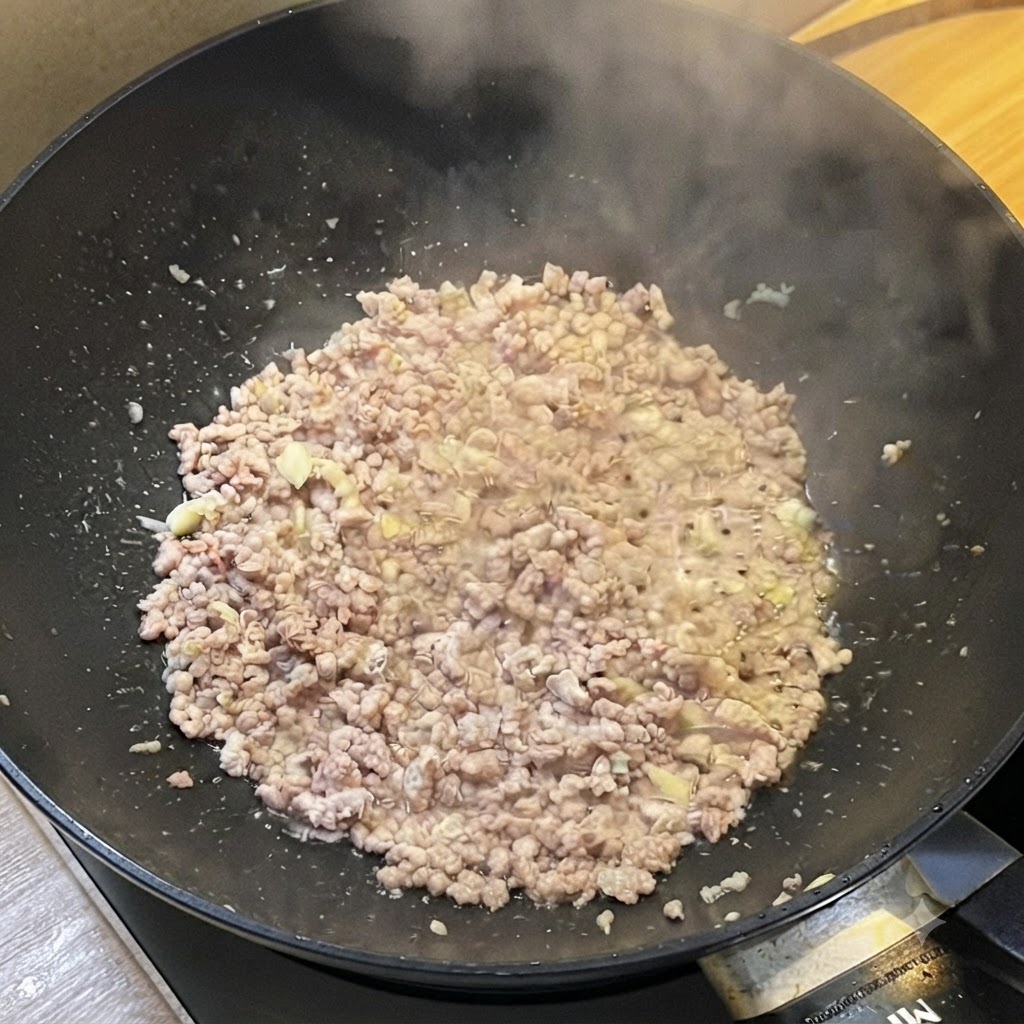 Un wok lleno de carne picada dorada que libera vapor mientras se sazona con salsas líquidas.