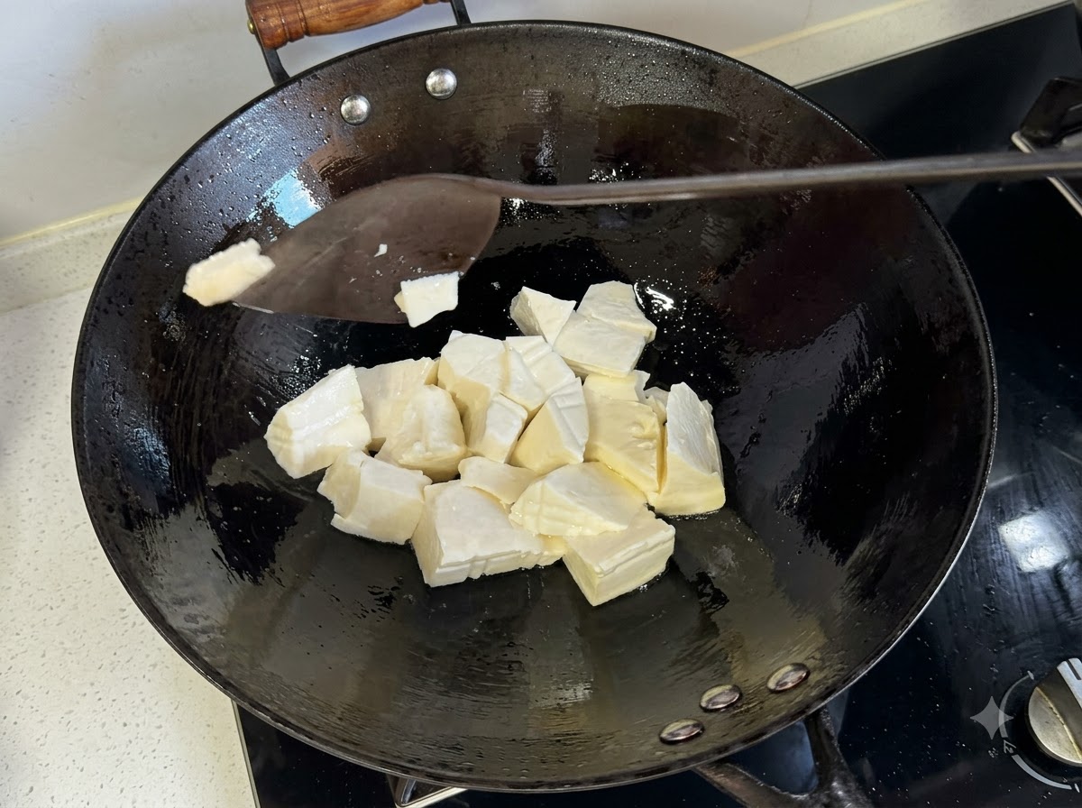 Una espátula cortando trozos de tofu suave dentro de un wok para freír caliente.