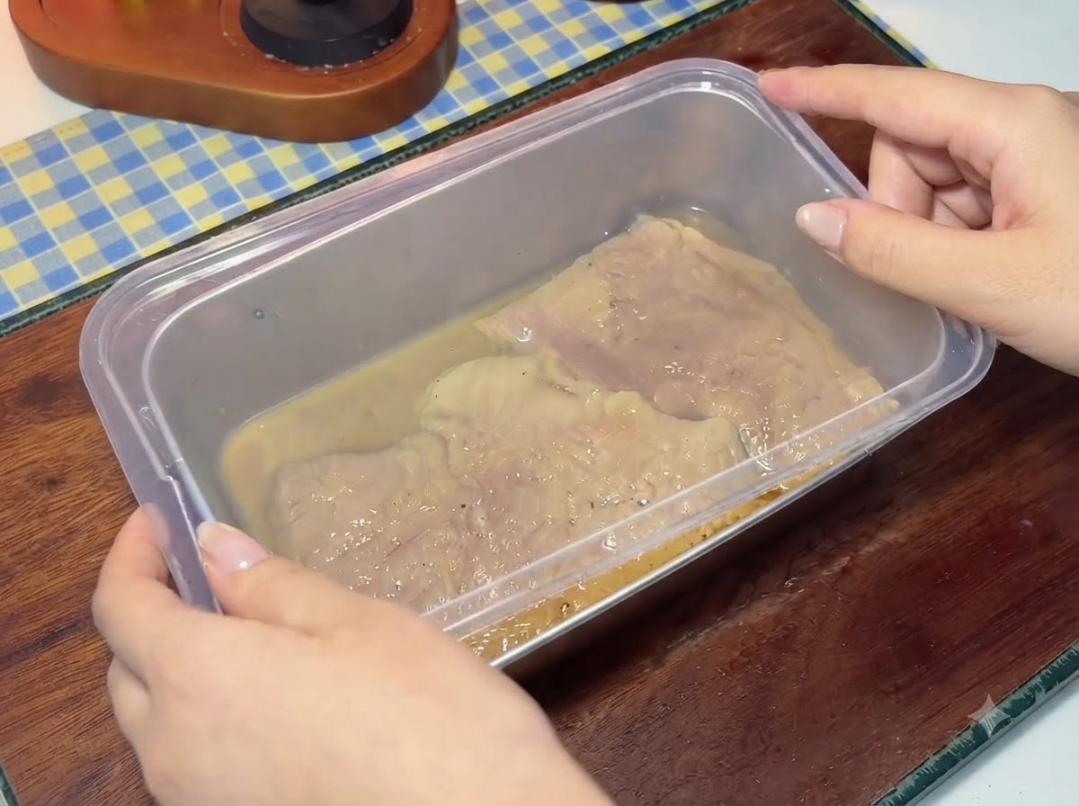 Colocando una tapa de plástico sobre un recipiente con chuletas de cerdo marinadas.